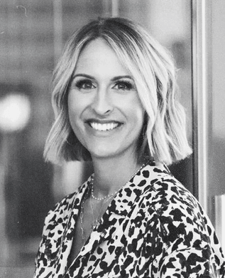 Stephany Kirkpatrick in a patterned blouse, smiling, by an office window