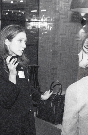 A founder in a dark coat and name tag talks with one hand raised, a handbag on her arm, at the club’s December evening event