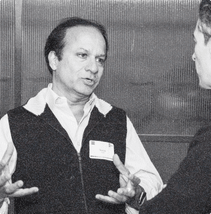 A founder in a vest and name tag gestures with both hands, mid conversation at the December event